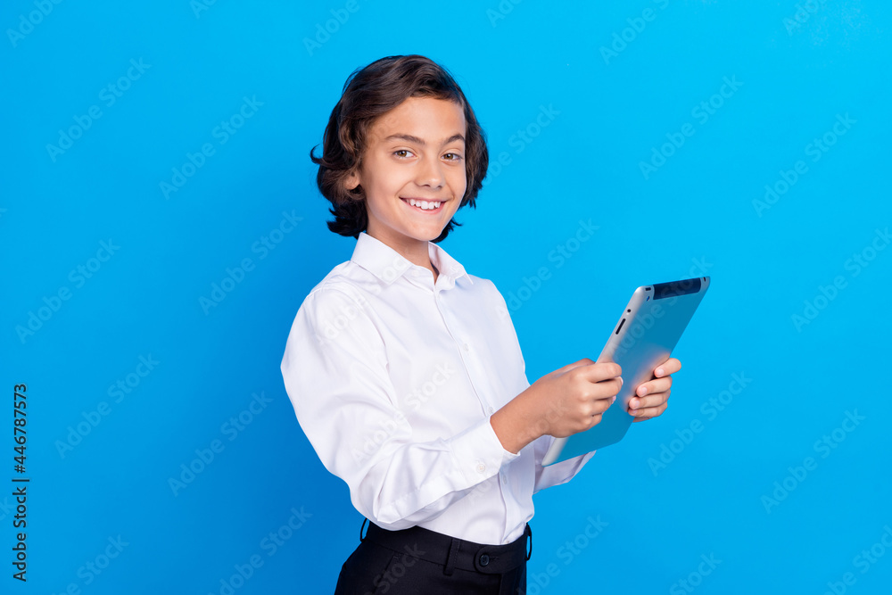 Photo of pretty sweet schoolboy wear formal clothes typing modern device smiling isolated blue color background Photo of pretty sweet schoolboy wear formal clothes typing modern device smiling isolated blue color background
