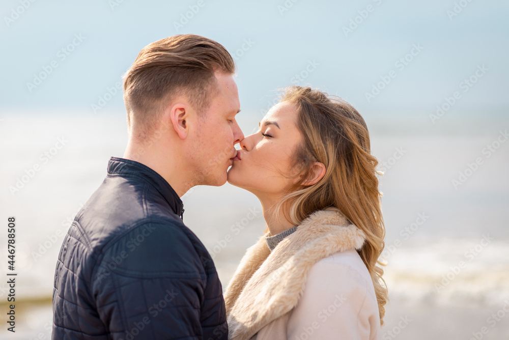 Young couple kissing outdoor.Stunning outdoors portrait of young stylish fashion couple posing in spring sea background. Young couple kissing outdoor.Stunning outdoors portrait of young stylish fashion couple posing in spring sea background.