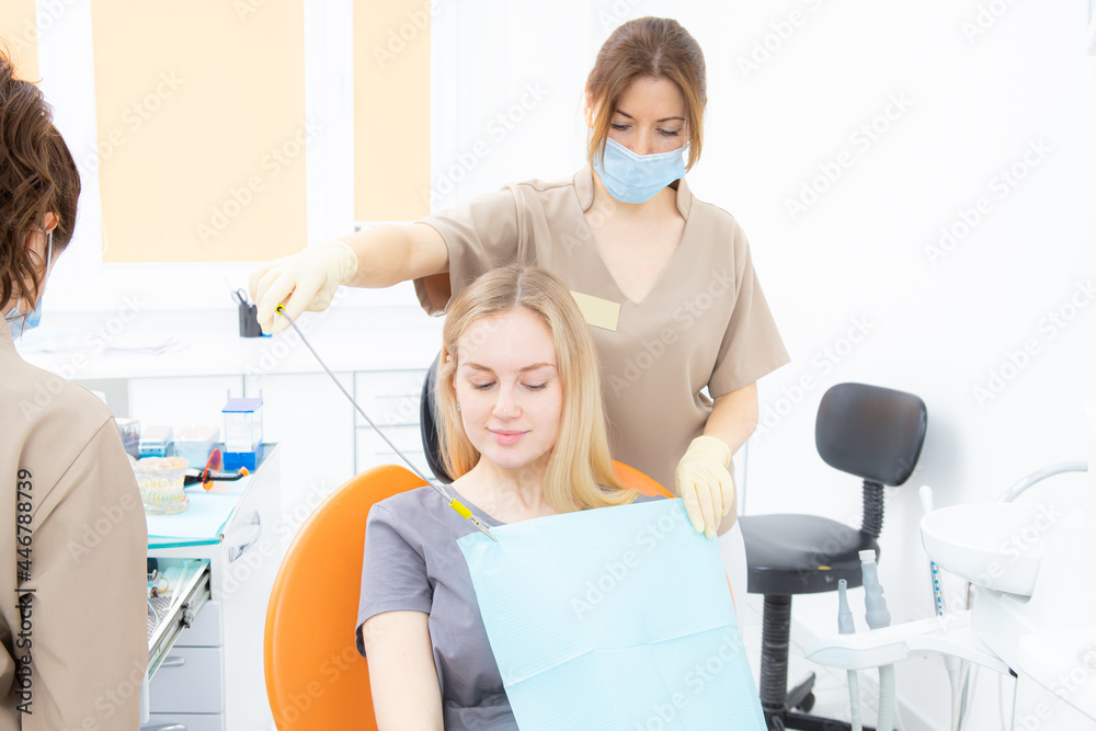 The dentist's assistant puts the protection on the patient before the treatment The dentist's assistant puts the protection on the patient before the treatment