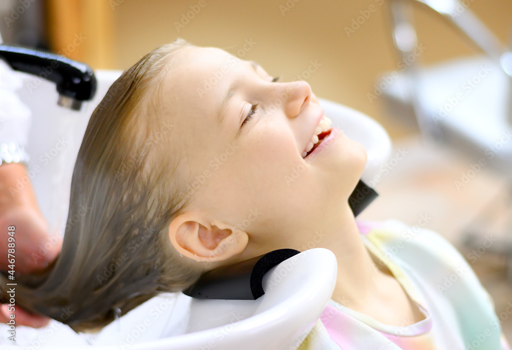 Fototapeta premium Portrait of a beautiful little girl in the hairdresser. Washing your hair with pleasure