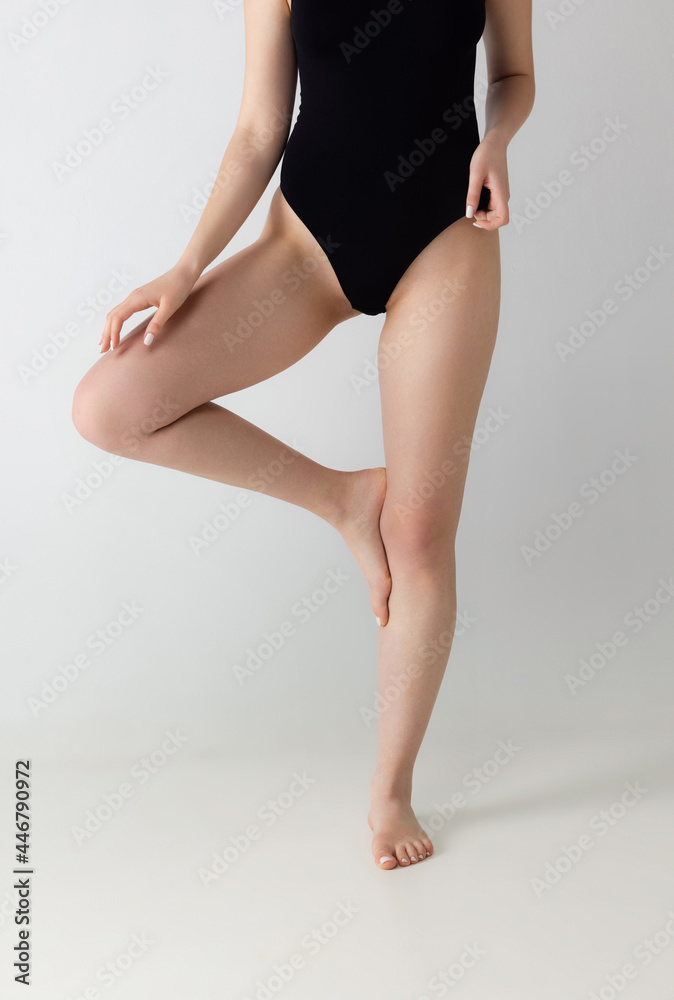 Slender female legs, body in black lingerie isolated over gray studio background. Natural beauty concept. Slender female legs, body in black lingerie isolated over gray studio background. Natural beauty concept.