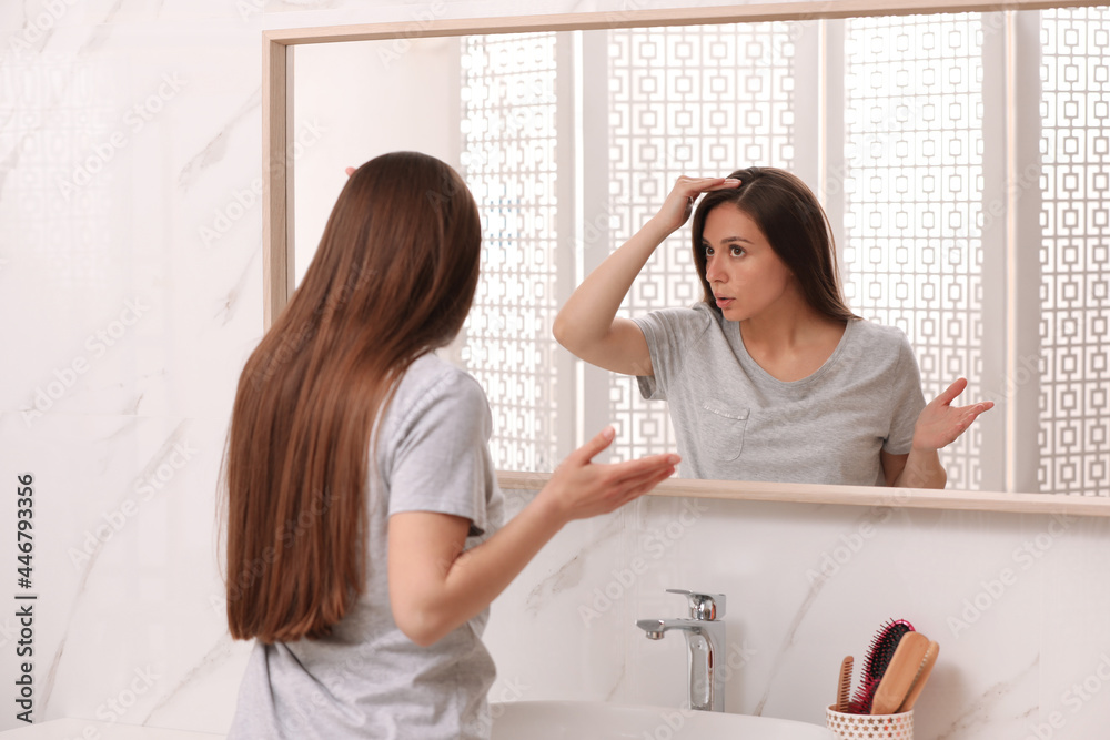 Young woman with hair loss problem looking near mirror in bathroom Young woman with hair loss problem looking near mirror in bathroom