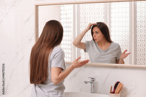 Young woman with hair loss problem looking near mirror in bathroom