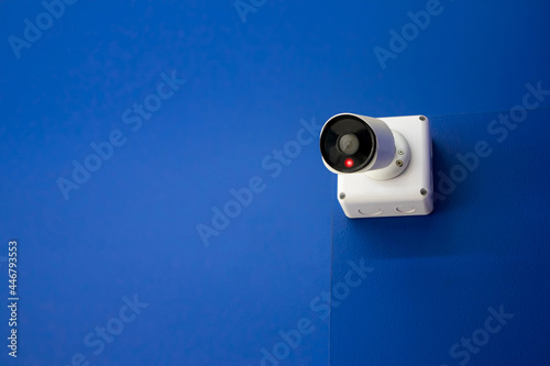 CCTV camera on blue concrete wall to record private or public spaces White Close Circuit Television is working by recording event with red indicator light for the duration of its operation