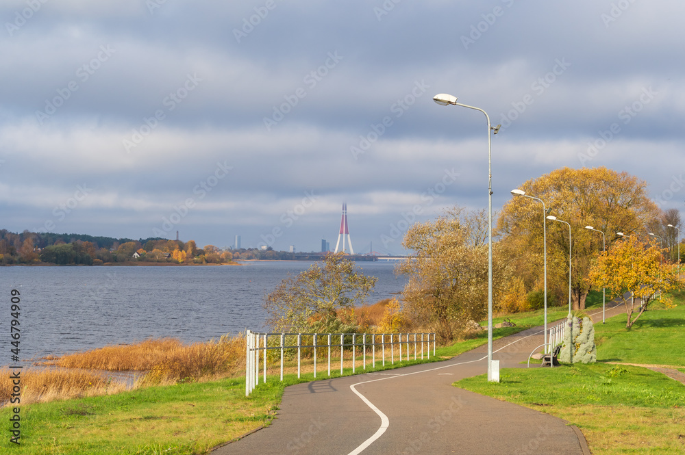 Daugava Promenade on sunny autumn day. River on the left side and colorful yellow trees by the river bank. Skyline in the horizon