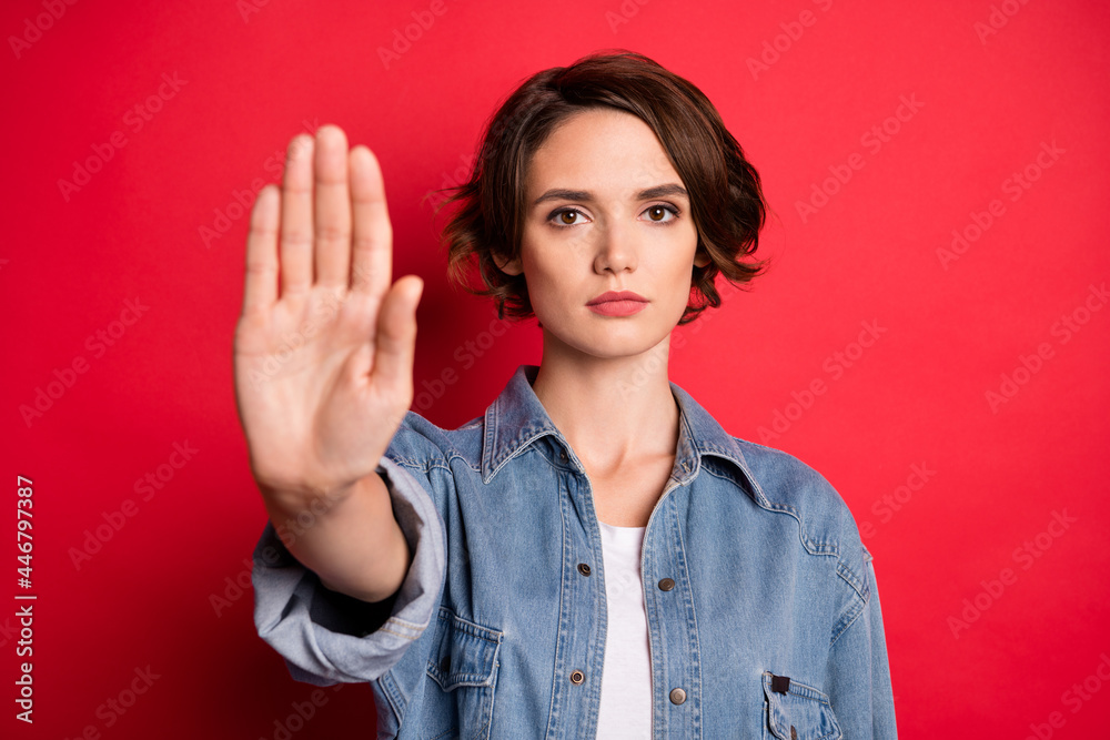 Photo of strict brunette millennial lady hand stop wear jeans shirt isolated on red color background Photo of strict brunette millennial lady hand stop wear jeans shirt isolated on red color background