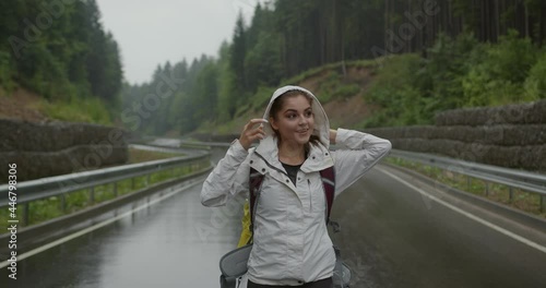 Attractive young woman in raincoat with backpack hiking among mountains during foggy weather. Pretty brunette enjoying outdoors activity alone. 