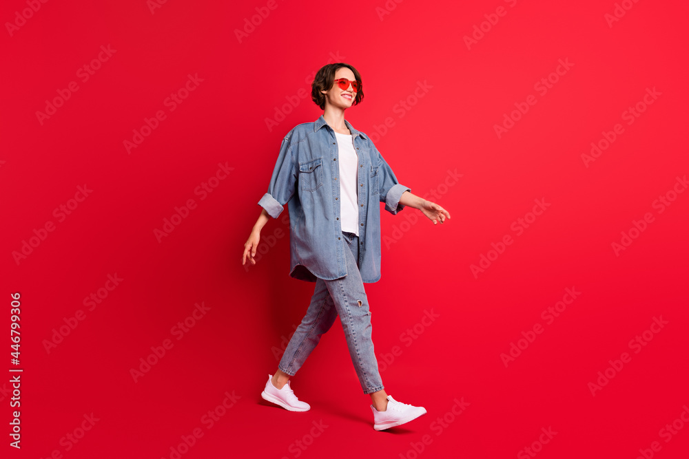 Full length body size photo girl wearing sunglass walking isolated vibrant red color background Full length body size photo girl wearing sunglass walking isolated vibrant red color background