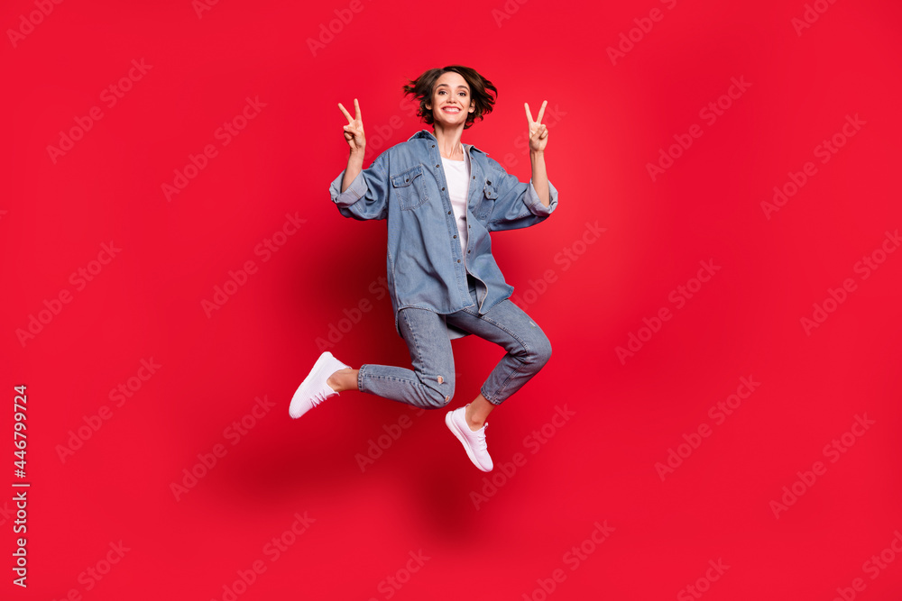 Full size photo of young woman happy positive smile show peace cool v-sign jump isolated over red color background