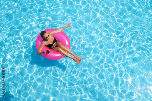 A beautiful young woman on an inflatable circle in blue water. Relaxing in the pool with a cocktail in hand