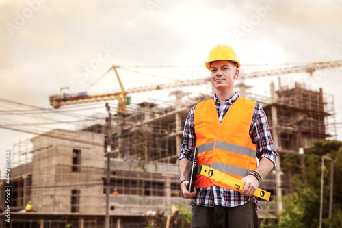 Handsome young man engineer holding laptop and construction level ruler with construction building background.