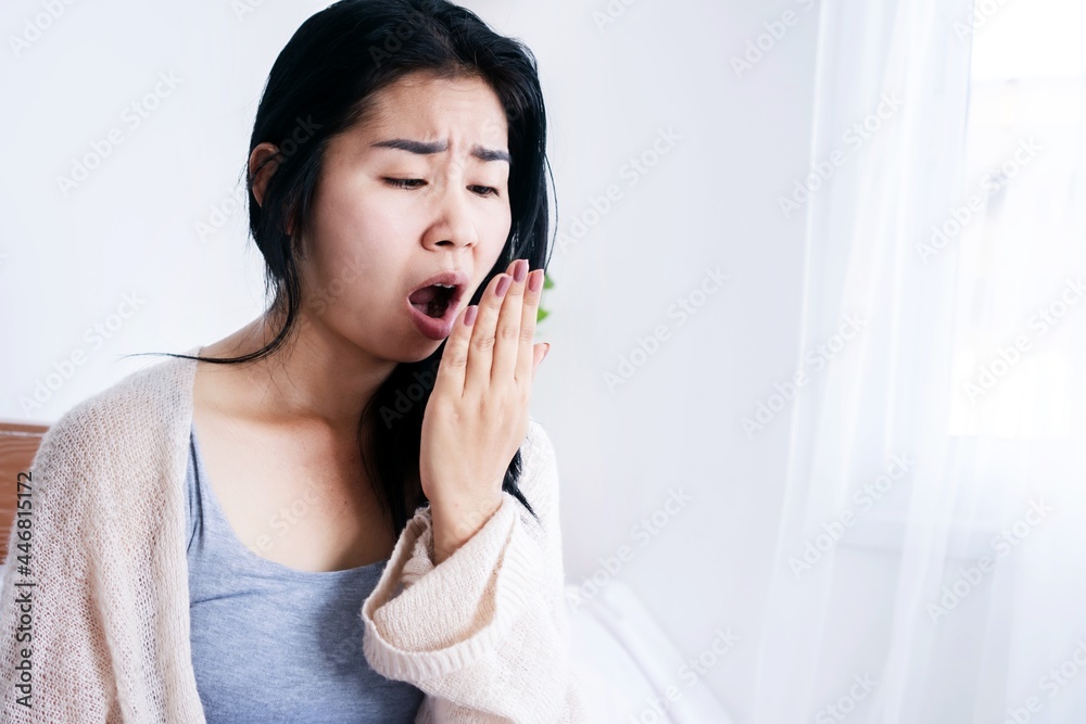 Asian woman sitting in bed open mouth checking her bad breath smell after wake up in the morning Asian woman sitting in bed open mouth checking her bad breath smell after wake up in the morning