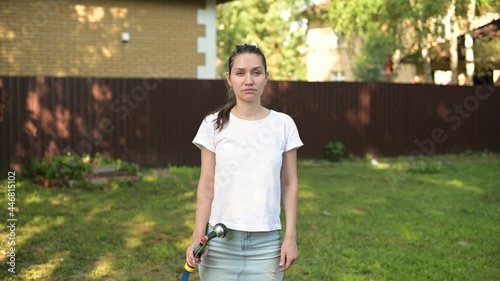 Young woman cools herself on a hot sunny day by pouring water from a garden hose, slow motion