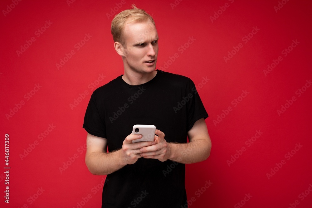 Handsome young man isolated over background wall wearing everyday clothes holding and using mobile phone writing sms looking to the side Handsome young man isolated over background wall wearing everyday clothes holding and using mobile phone writing sms looking to the side