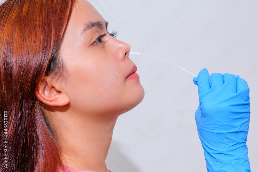 Woman wearing blue medical gloves and emakes with a cotton swab a nasal swab test holding COVID-19 (SARS-CoV-2) First Antigen Test kit device to help in the Rapid Detection testing at home. Woman wearing blue medical gloves and emakes with a cotton swab a nasal swab test holding COVID-19 (SARS-CoV-2) First Antigen Test kit device to help in the Rapid Detection testing at home.