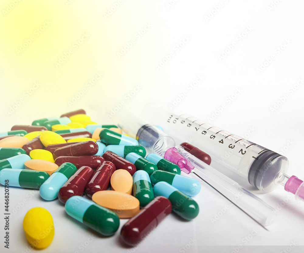 Various medicine pills, orange tablets, blue and green capsules, and injection syringe on white background, soft and selective focus Various medicine pills, orange tablets, blue and green capsules, and injection syringe on white background, soft and selective focus