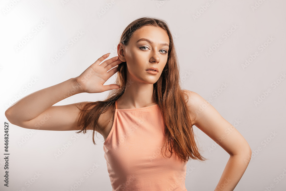 Fototapeta premium Beautiful young girl holds his hand near his ear, wants to hear better on a white background with a place for advertising mockup