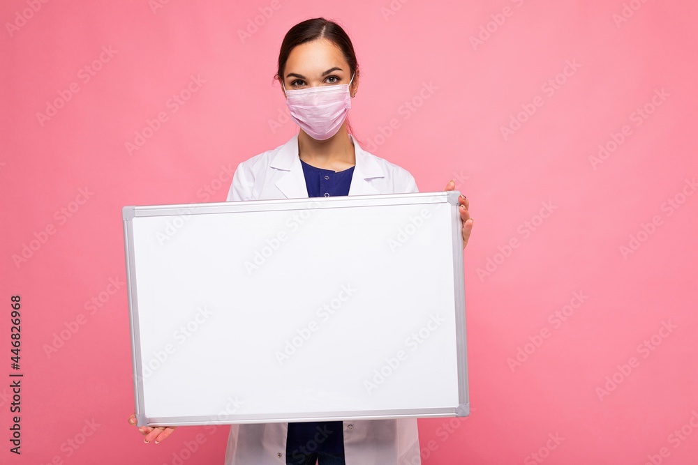 Woman doctor wearing a white medical coat and a mask holding blank board with copy space for text isolated on background. Coronavirus concept Woman doctor wearing a white medical coat and a mask holding blank board with copy space for text isolated on background. Coronavirus concept