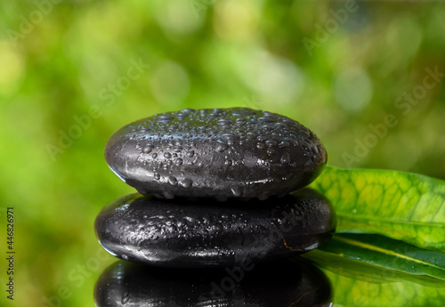 Spa massage stones on a fresh green background stock images. Spa and wellness frame stock images. Pile of black stones photo. Spa-concept with zen stones with copy space for text