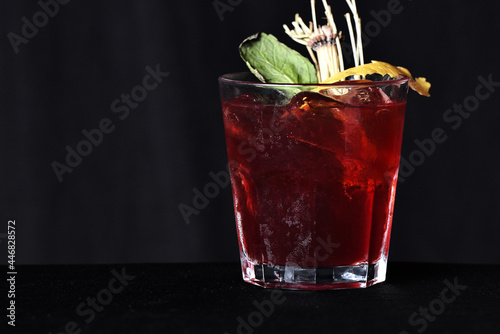 refreshing alcoholic drink with berries, ice vodka and gin, lemon peel served in glass cup on the counter on black background