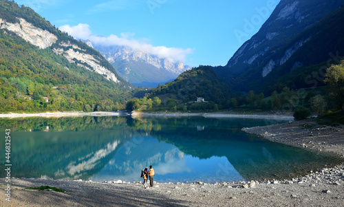 Lago di Tenno with its clear water in the morning light. Two people standing on the bank. Trentino, Italy.