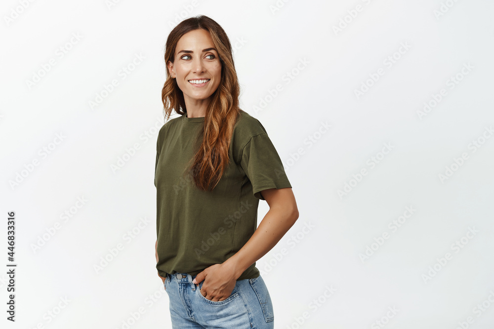 Portrait of young attractive middle-aged woman smiling, looking behind her shoulder, right side sale banner, smile pleased, standing in t-shirt and jeans against white background Portrait of young attractive middle-aged woman smiling, looking behind her shoulder, right side sale banner, smile pleased, standing in t-shirt and jeans against white background