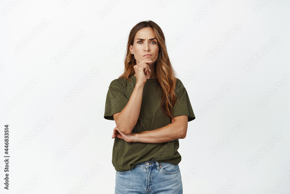 Portrait of serious middle aged woman thinking, furrow eyebrows and looking displeased at camera, standing thoughtful against white background Portrait of serious middle aged woman thinking, furrow eyebrows and looking displeased at camera, standing thoughtful against white background