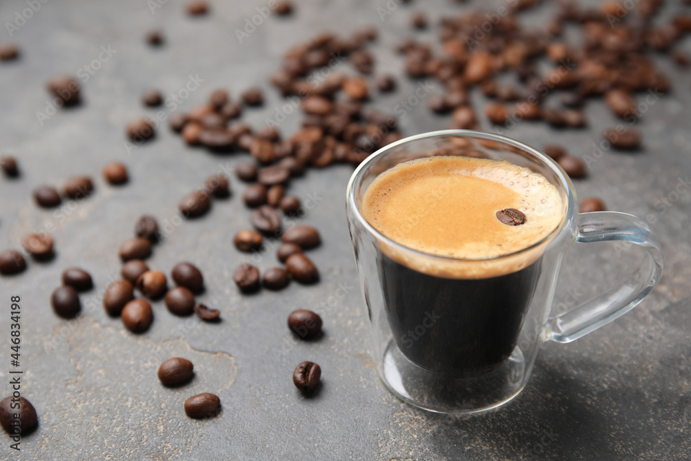 Cup of tasty espresso and scattered coffee beans on grey table. Space for text Cup of tasty espresso and scattered coffee beans on grey table. Space for text