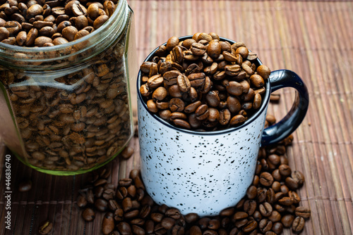 Mug and glass jar with coffee beans on bamboo background