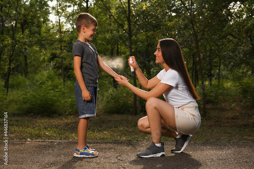 Woman applying insect repellent on her son's arm in park. Tick bites prevention photo