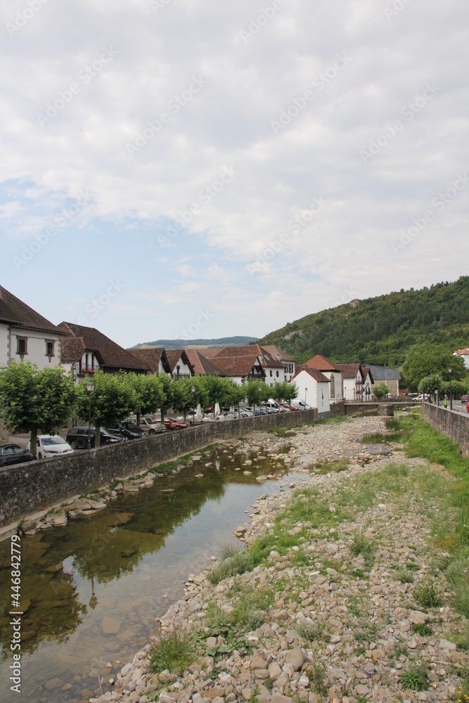 River with stones and vegetation and typical houses with a cloudy sky in Otsagabia, Navarra