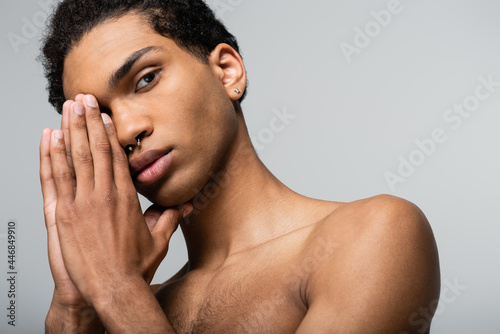 african american guy posing with hands near face while looking at camera isolated on grey, beauty concept