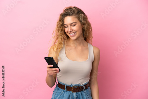 Young blonde woman isolated on pink background sending a message or email with the mobile