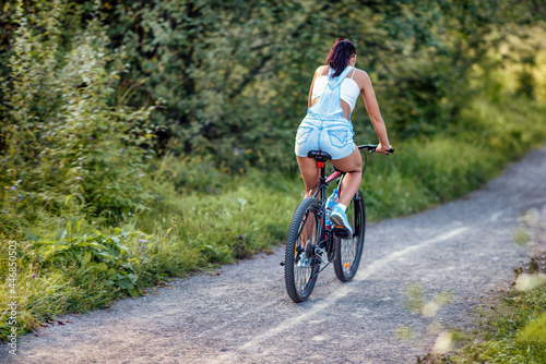 A young woman riding a bicycle in a park in summer.