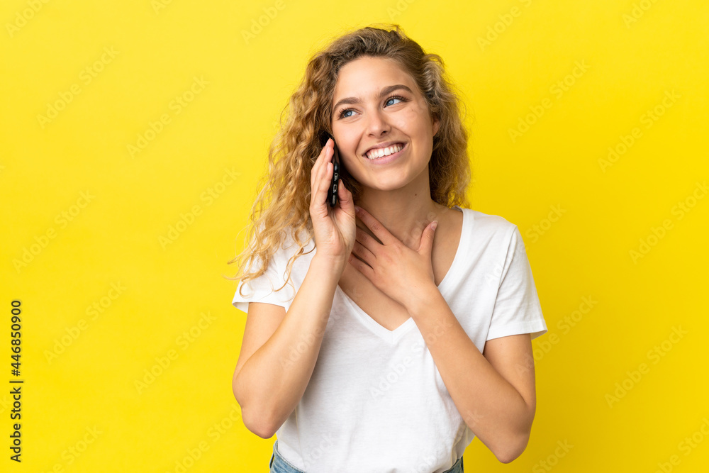 Young blonde woman using mobile phone isolated on yellow background looking up while smiling Young blonde woman using mobile phone isolated on yellow background looking up while smiling