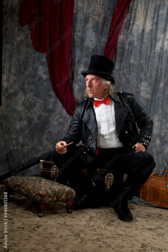 Naklejka premium Portrait of victorian steampunk, looking away, wearing top hat, tail coat, bow tie and sitting on trunk.