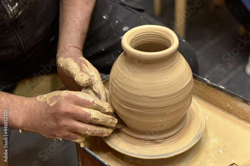 Hands of a ceramist in the process of making a large vase of light clay on a potter's wheel