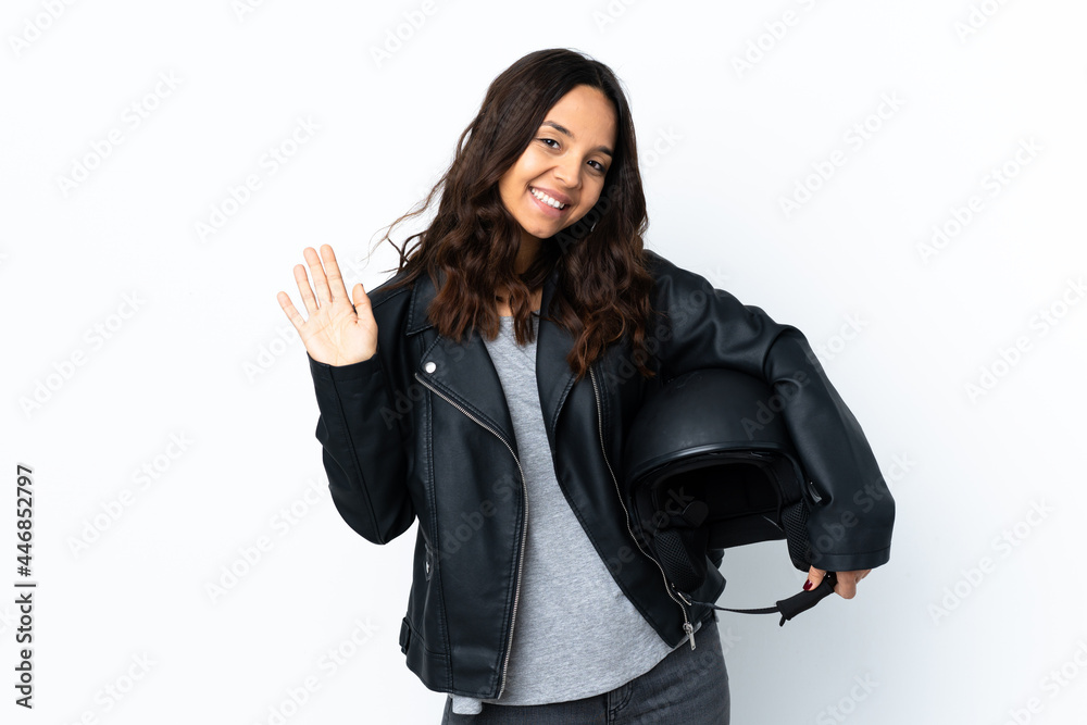 Young woman holding a motorcycle helmet over isolated white background saluting with hand with happy expression Young woman holding a motorcycle helmet over isolated white background saluting with hand with happy expression
