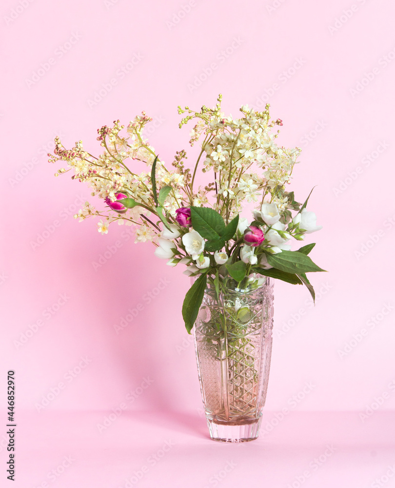 Bouquet of meadowsweet (Latin Filipndula), jasmine and wild roses in a vase on a pink background.	