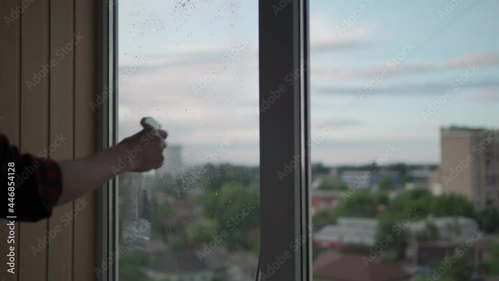 Washing window glass at home. A young long-haired man with a beard is cleaning the apartment. Sanitary worker is disinfecting panoramic windows in an empty room. purity, cleanliness, change concept