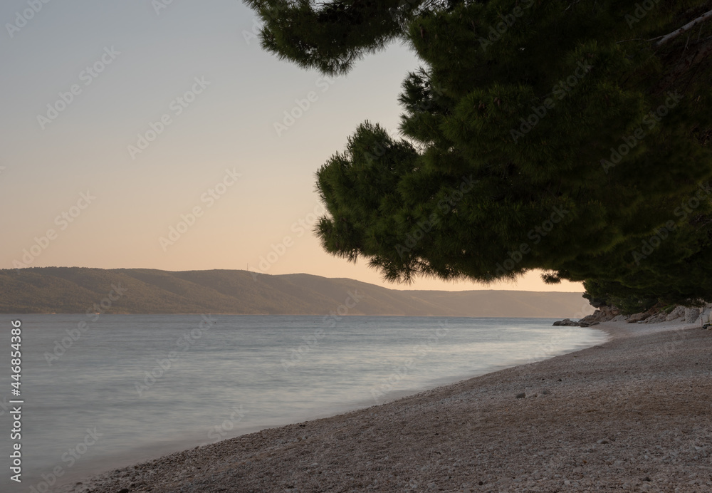 Naklejka premium Beach on the shore of Adriatic Sea during sunset. Zivogosce, Makarska Riviera, Dalmatia, Croatia. Long exposure, selective focus. 