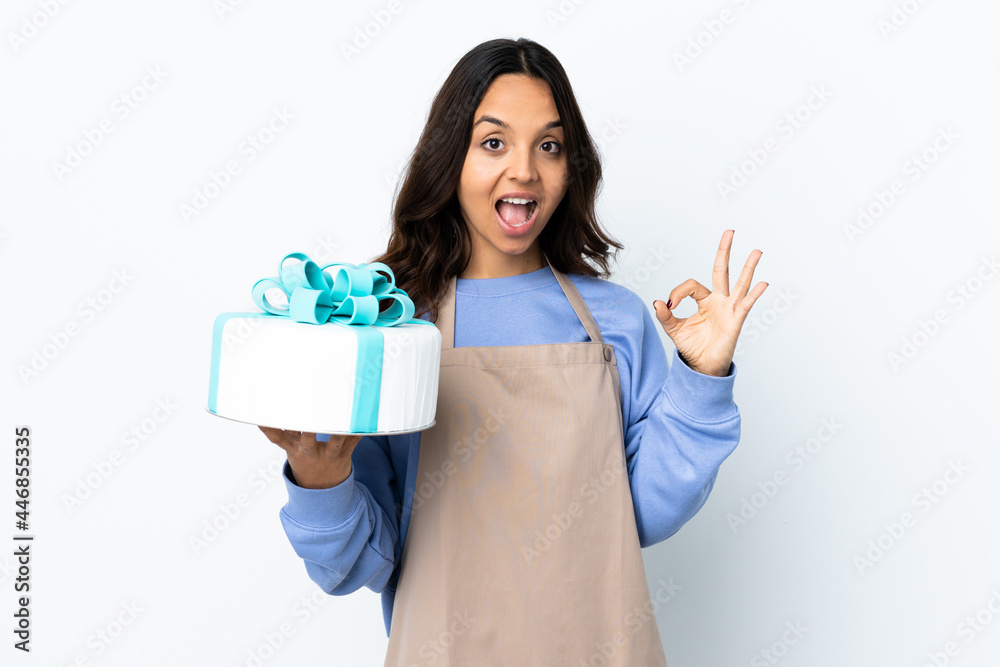 Pastry chef holding a big cake over isolated white background showing ok sign and thumb up gesture Pastry chef holding a big cake over isolated white background showing ok sign and thumb up gesture