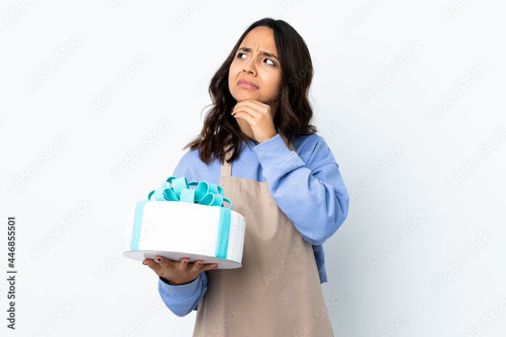 Pastry chef holding a big cake over isolated white background having doubts and with confuse face expression Pastry chef holding a big cake over isolated white background having doubts and with confuse face expression