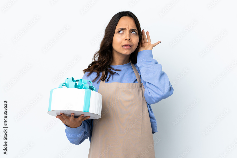 Pastry chef holding a big cake over isolated white background listening to something by putting hand on the ear Pastry chef holding a big cake over isolated white background listening to something by putting hand on the ear