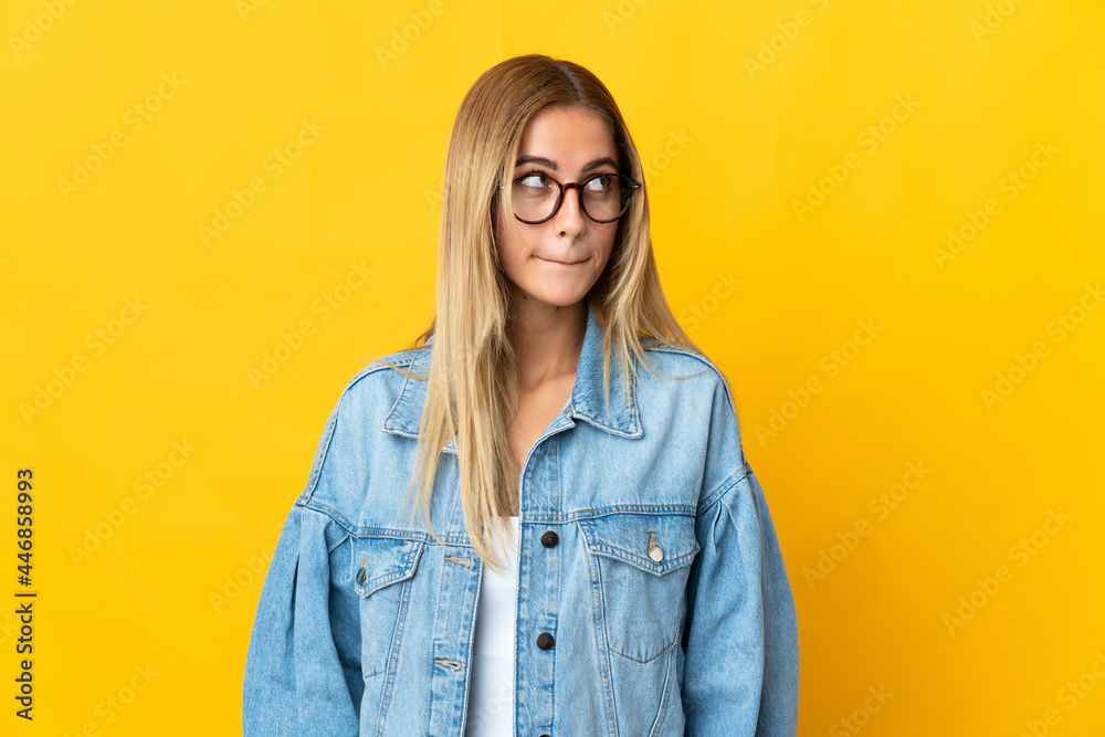 Young blonde woman isolated on yellow background having doubts while looking up
