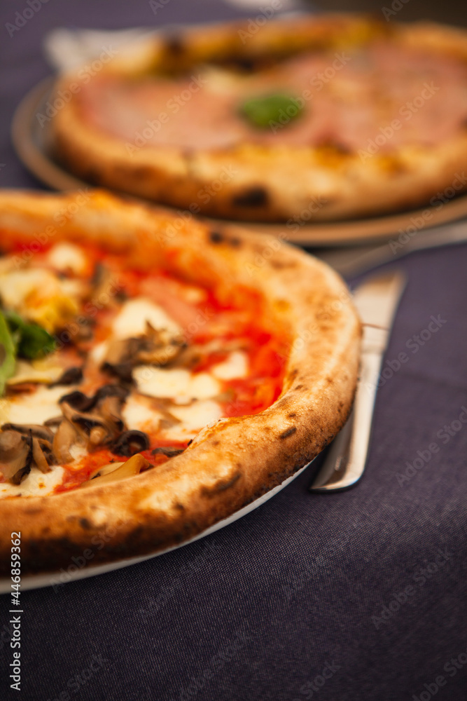 Close up. Two traditional Italian round pizzas with prosciutto, mushrooms, ham, pistachio, olives, basil and mozzarella cheese at the restaurant in Milan, Lombardy, Italy. European food and snacks. 