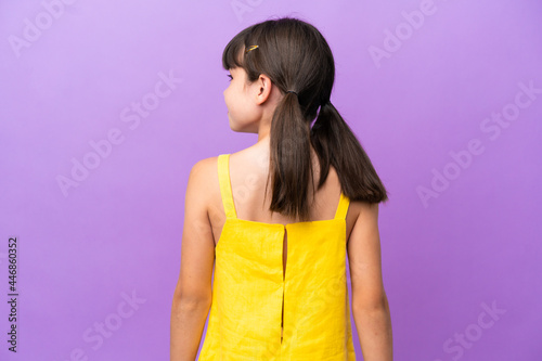 Little caucasian kid isolated on purple background in back position and looking side