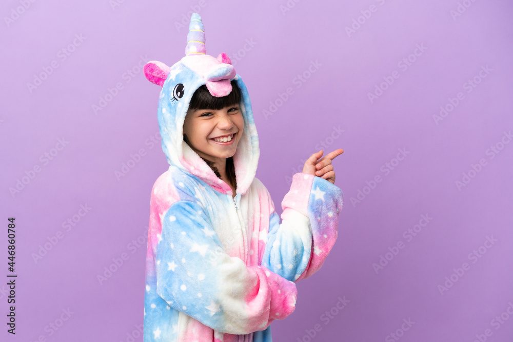 Little kid wearing a unicorn pajama isolated on purple background pointing finger to the side Little kid wearing a unicorn pajama isolated on purple background pointing finger to the side