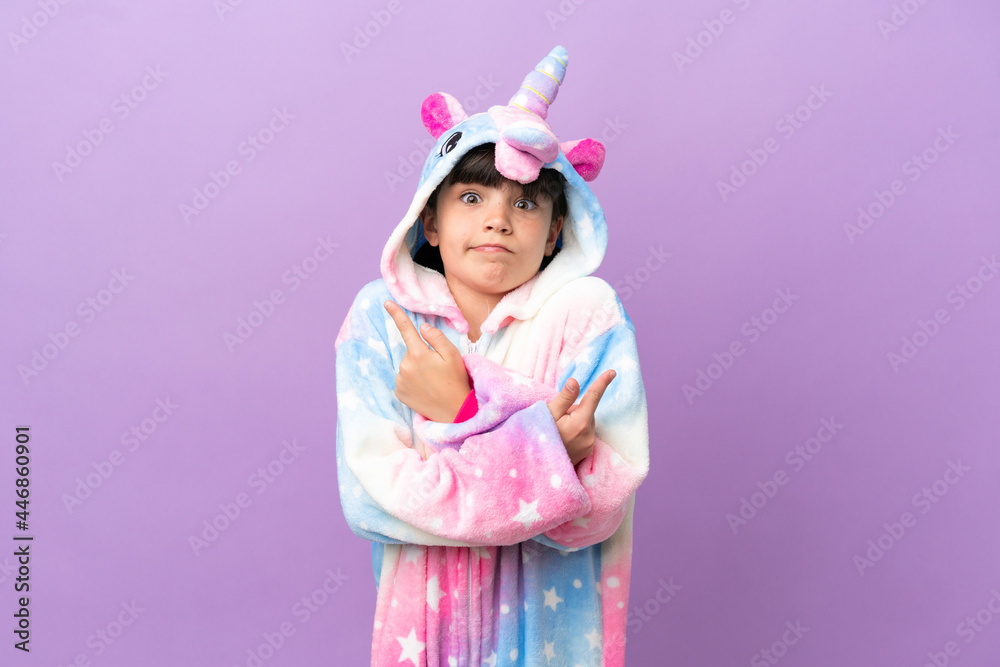Little kid wearing a unicorn pajama isolated on purple background pointing to the laterals having doubts Little kid wearing a unicorn pajama isolated on purple background pointing to the laterals having doubts