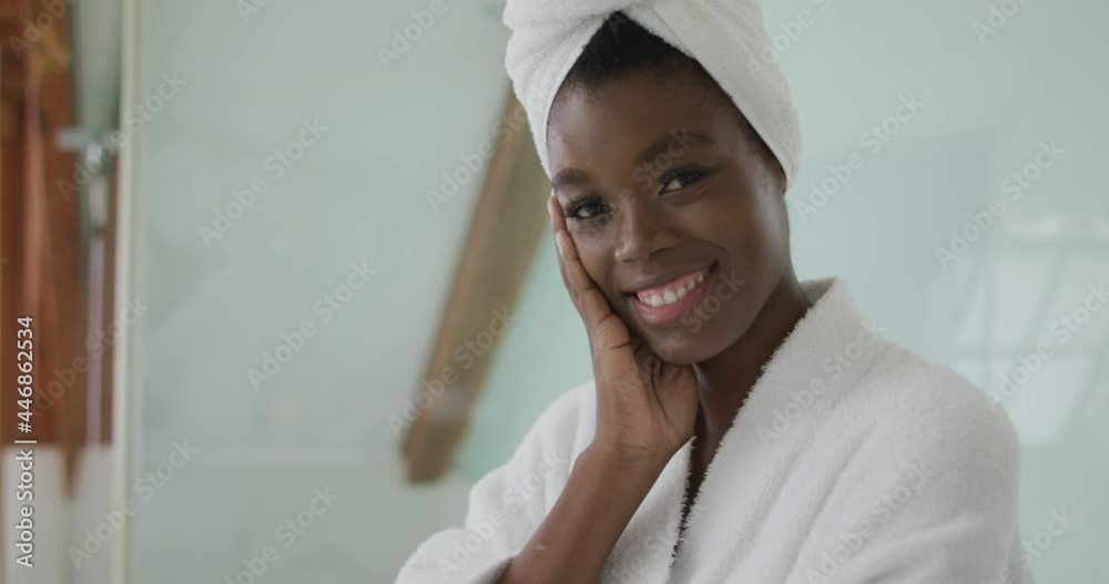 Portrait of smiling african american attractive woman wearing robe and turban in bathroom